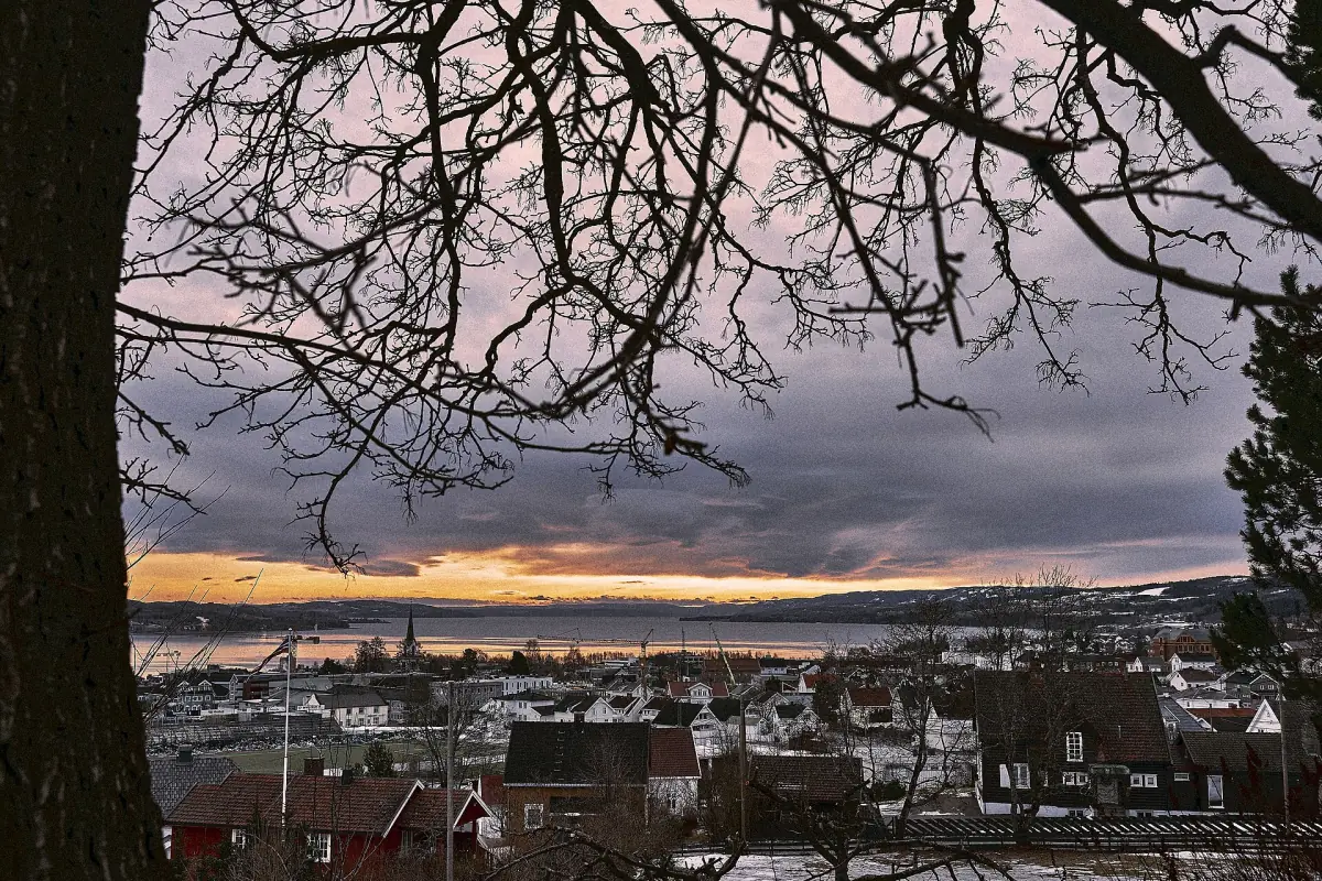 Kveldsglød over Gjøvik og Mjøsa sett gjennom bare greiner fra åssiden