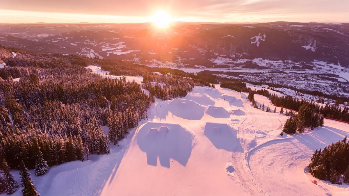 Soloppgang over snødekte bakker og en terrengpark i Hafjell skisenter
