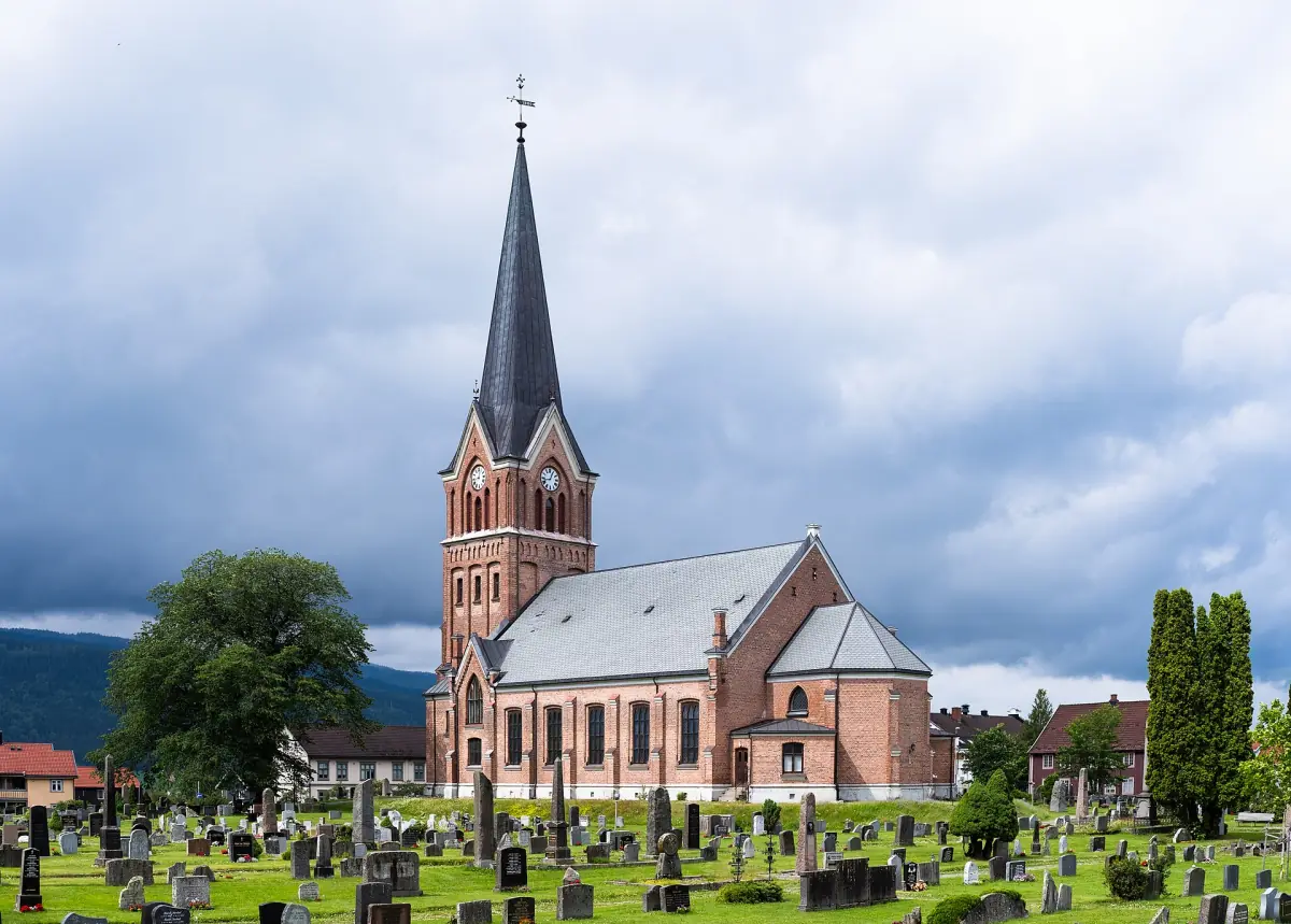 Murkirke med høyt spir og kirkegård i Lillehammer en solfylt dag
