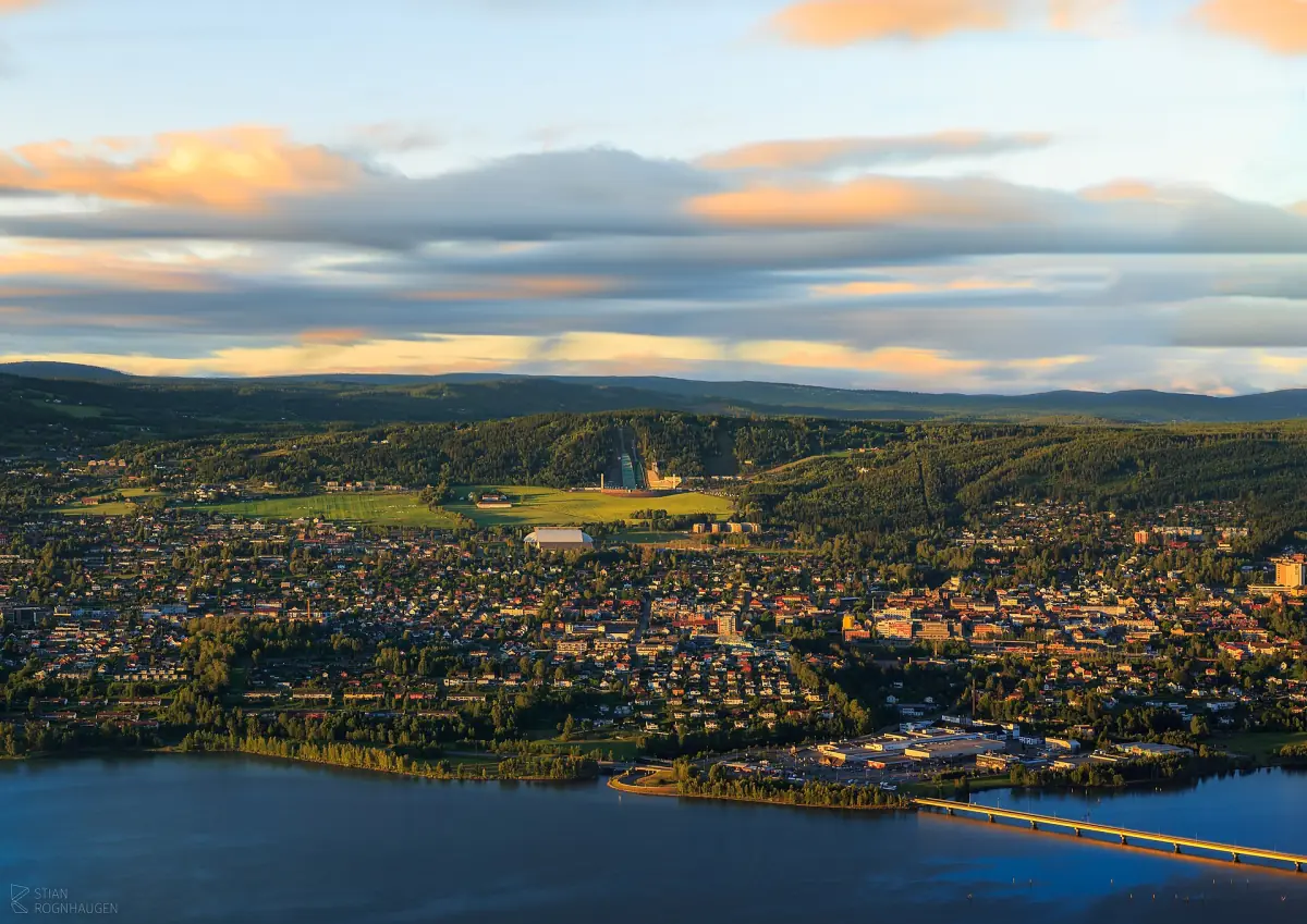 Flyfoto av Lillehammer og bredden av Mjøsa i skumringen med oransje skyer