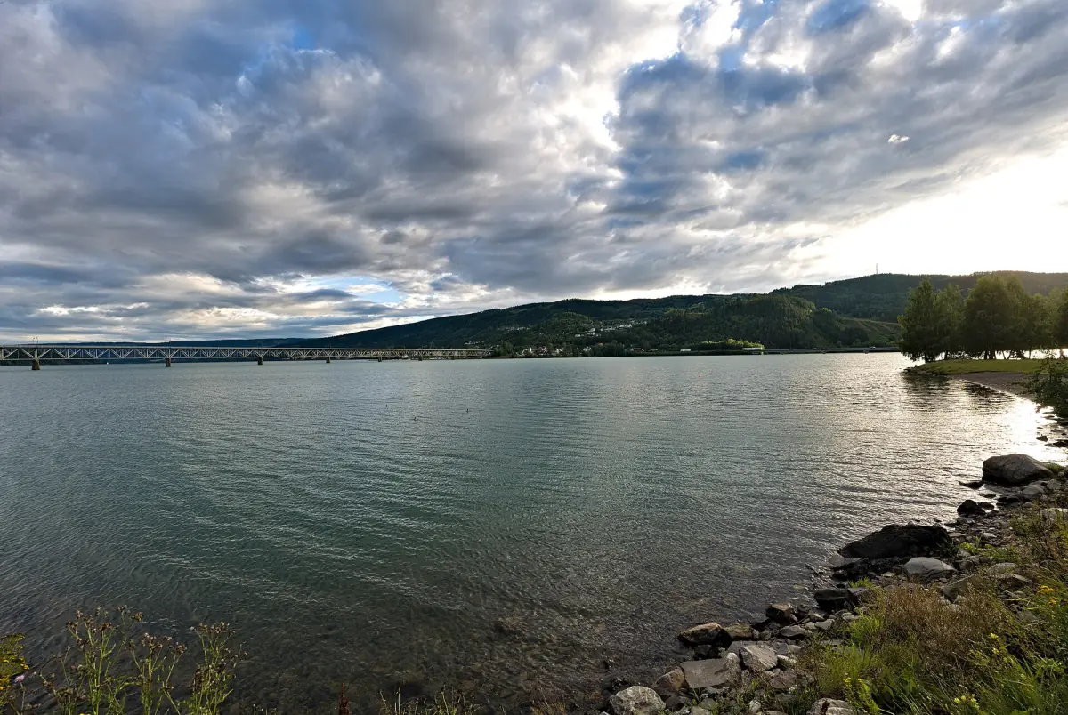 Rolig Mjøsa sett fra strandpromenaden i Lillehammer under spredte skyer
