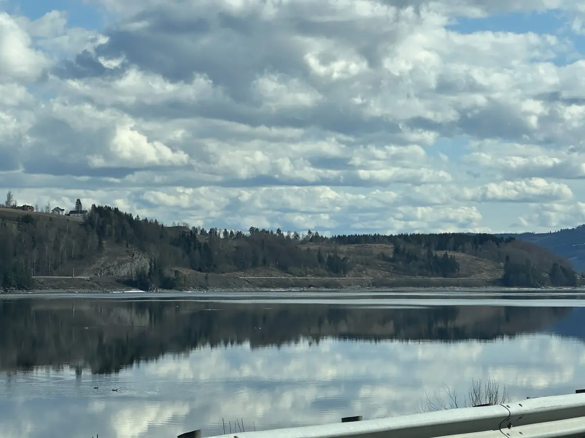 Stille Mjøsa speiler skyer og skogkledd bredd sør for Vingnes ved Lillehammer