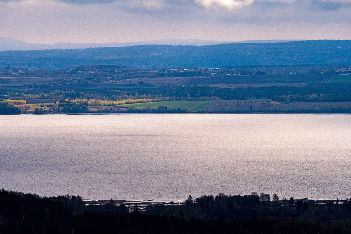 Den brede rolige Mjøsa med jordbruksland og fjerne åser ved Stange i skumringen