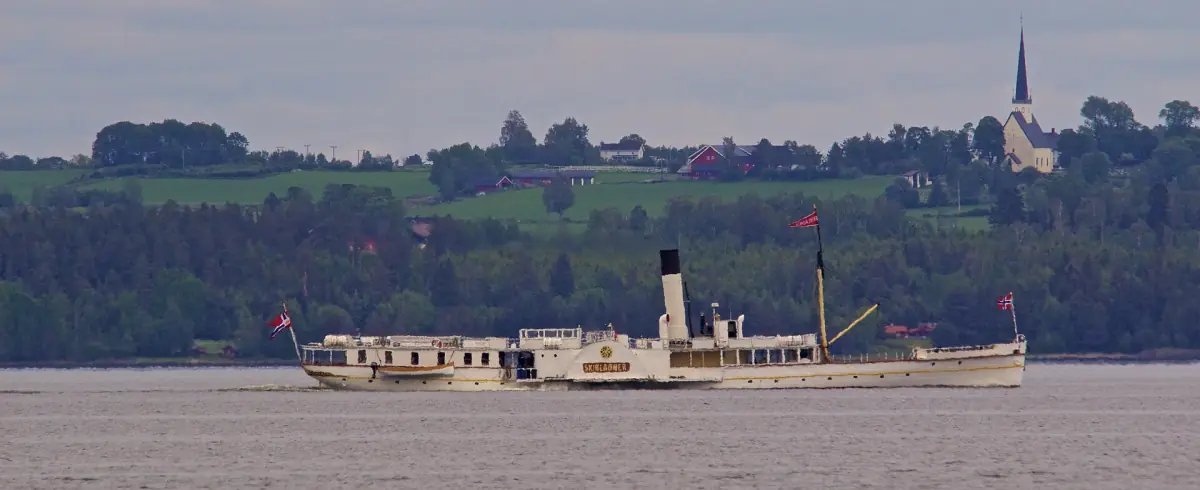 Skibladner på Mjøsa foran grønne åser og et kirkespir ved Stange