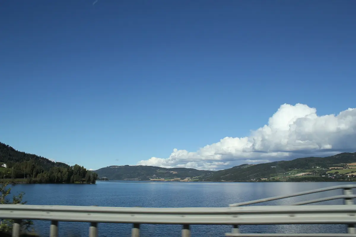 Utsikt fra Mjøsbrua over blå Mjøsa og skogkledde åser med hvite skyer